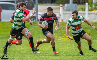 Rugby player running with the ball while being chased by 2 guys on either side of him